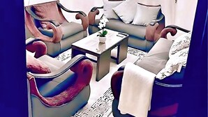 A modern living room with a sofa set, a coffee table, a TV mounted on the wall, and a ceiling fan. - Elegant Apartment -Sheikh Zayed Compound (Sheikh Zayed)