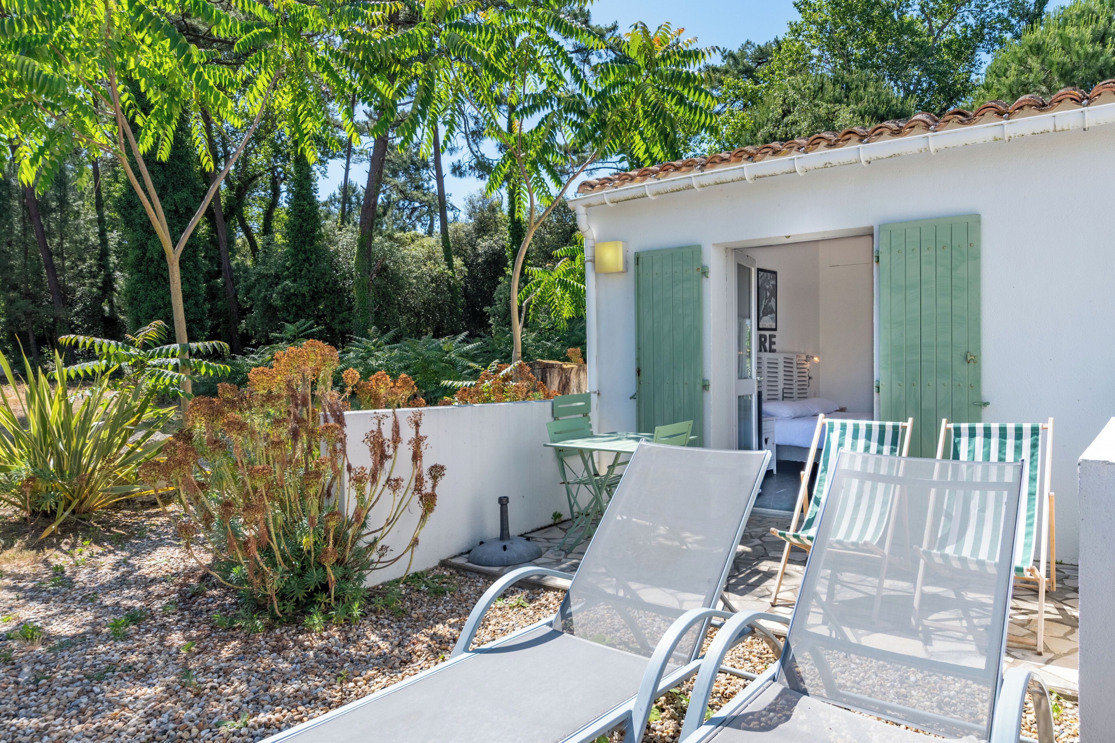 Una casa pequeña con jardín, mobiliario exterior y una puerta que da a una habitación.