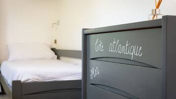 Une chambre à coucher avec un lit, une commode portant une plaque nominative et une lampe fixée au mur.
