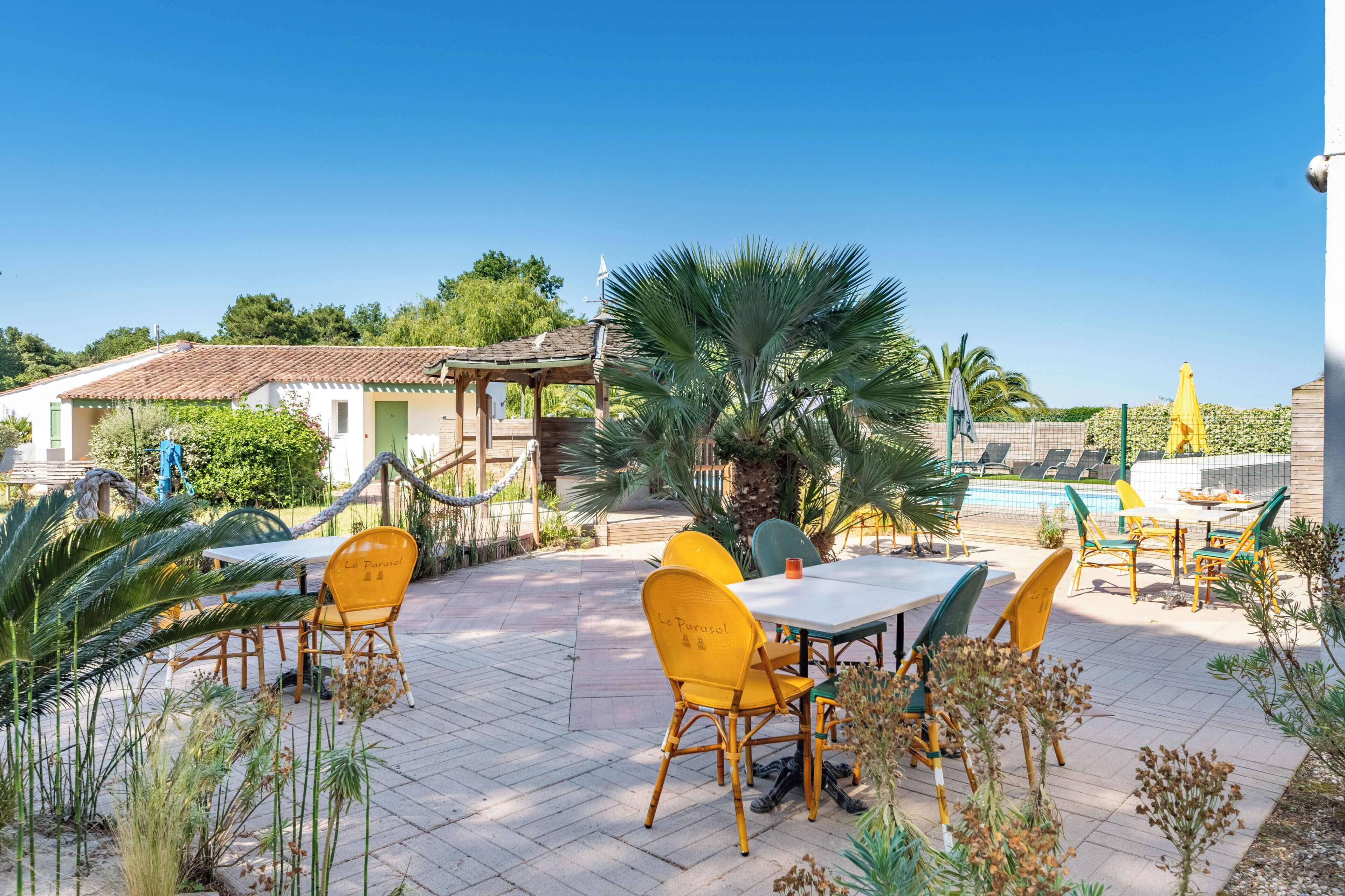 An outdoor patio with tables and chairs, a pool, and a covered area.