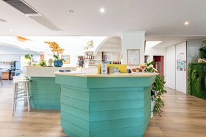A modern interior with a teal-colored reception desk, a white wall with a framed menu, and a wooden floor. - Le Parasol (Ars-en-Ré)