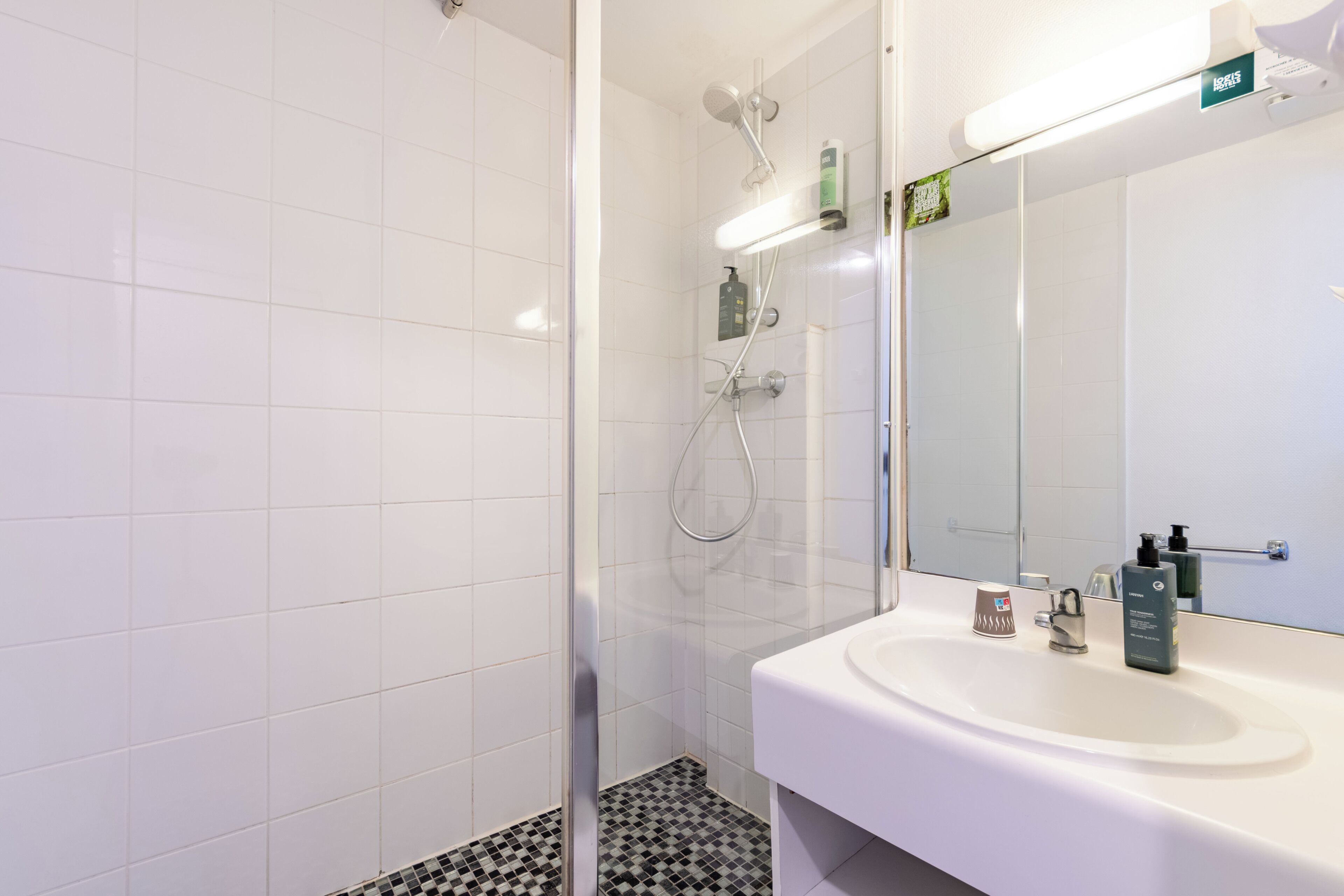 A modern bathroom with a glass shower enclosure, a white sink with a mirror, and a tiled floor.