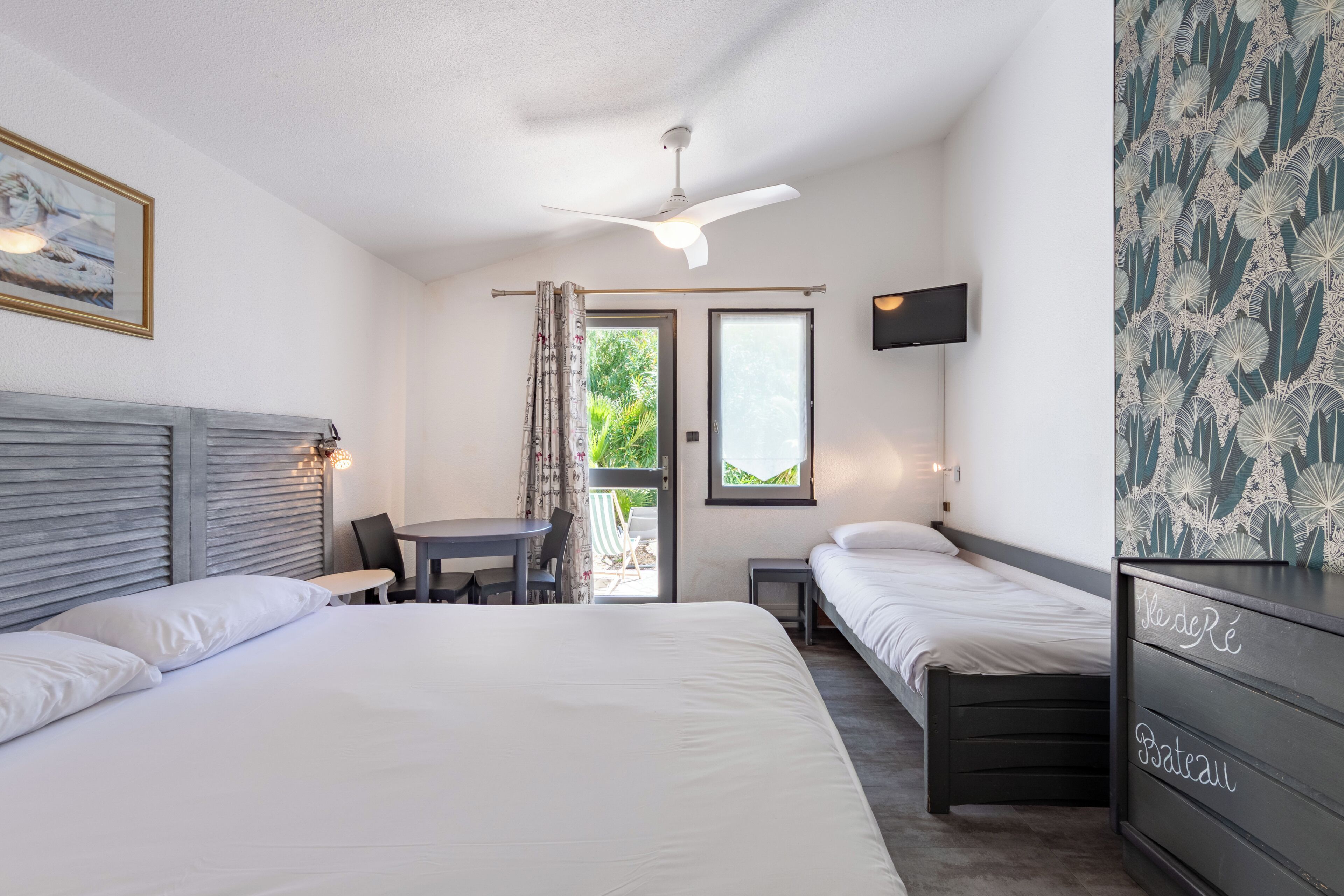 A hotel room with two beds, a dining table, a TV, and a balcony with a view.