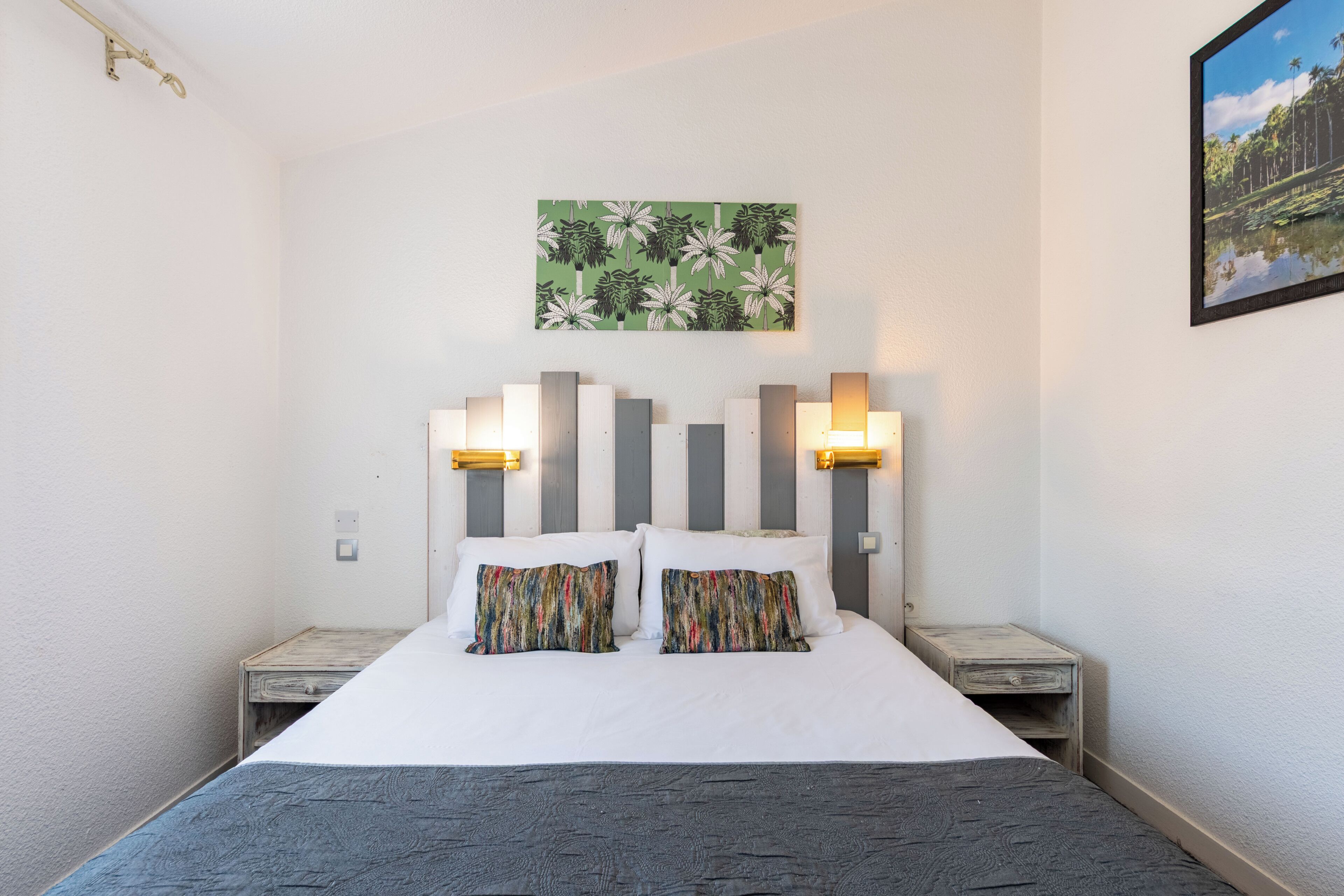 A neatly made bed with a striped headboard, two bedside tables, and a wall-mounted painting.