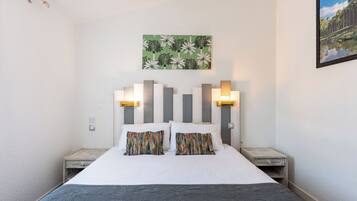 A neatly made bed with a striped headboard, two bedside tables, and a wall-mounted painting.