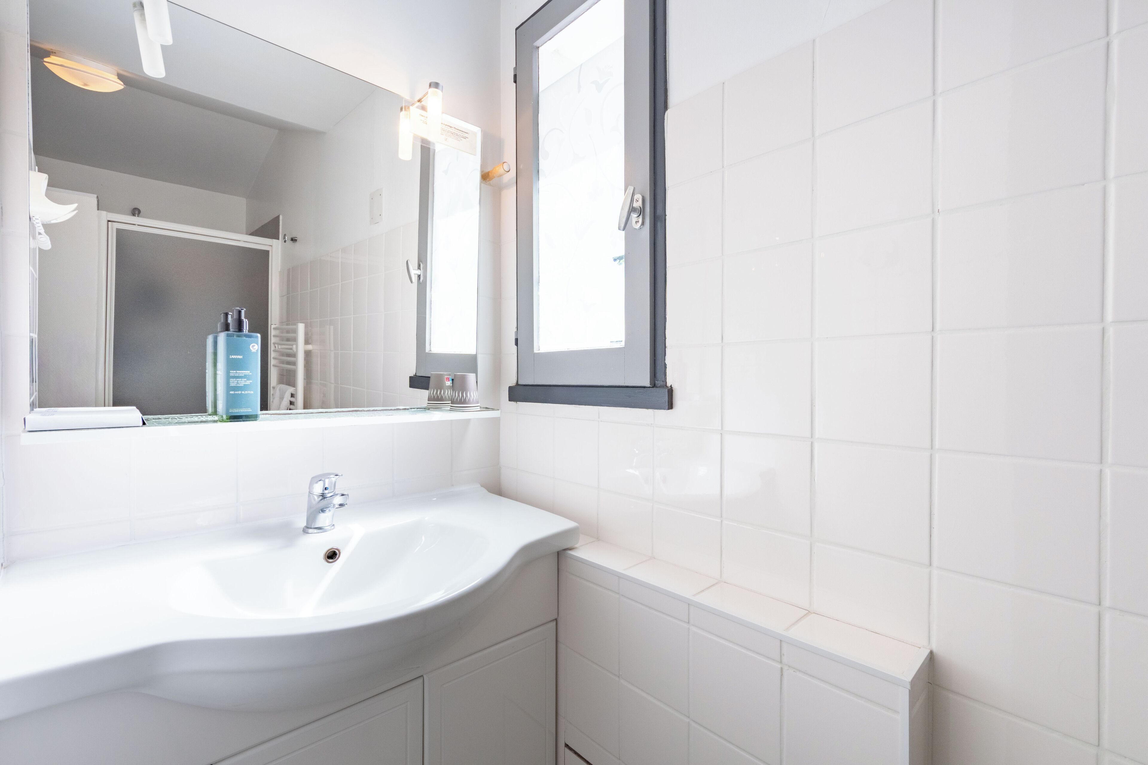 A bathroom with a white sink, a mirror, and a window.