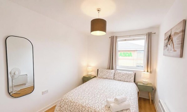 A bedroom with a bed, a mirror, a window with curtains, a wall-mounted radiator, and a wall-mounted artwork. - Exclusive 1 Bedroom Flat with CAR PARKING! (Greater London)