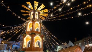 Ein mit Lichtern beleuchtetes Riesenrad mit vielen Menschen.