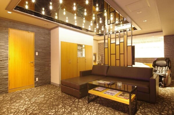 Una habitación de hotel moderna con sofá, sillón de masaje, mesa de centro de vidrio y suelo estampado.
