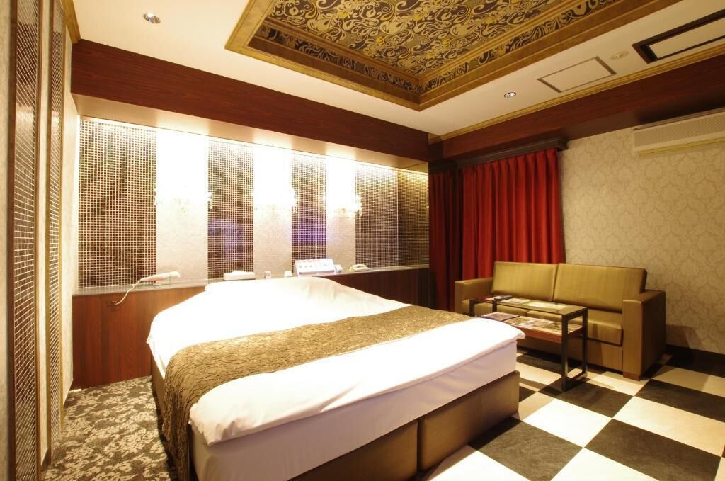 Une chambre d’hôtel avec un grand lit, un canapé, une petite table et une fenêtre avec des stores.