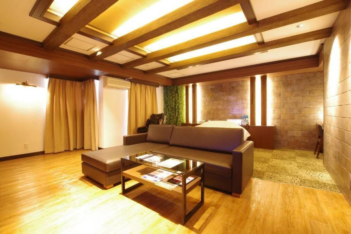 A modern hotel room with a wooden ceiling, a sofa, a glass coffee table, and a stone wall.