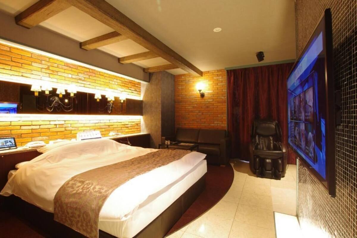 A hotel room with a bed, a desk with a computer, a TV, and a massage chair.