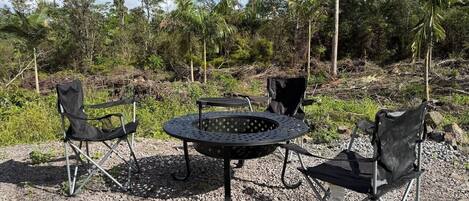 An outdoor seating area with a metal fire pit table and four black folding chairs.