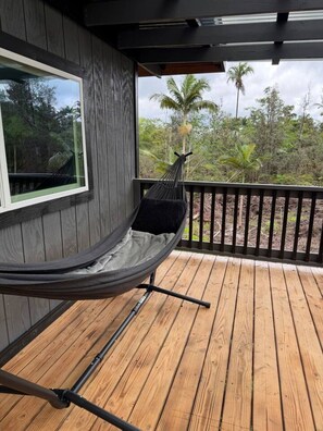 A hammock on a wooden deck with a view of tropical vegetation.