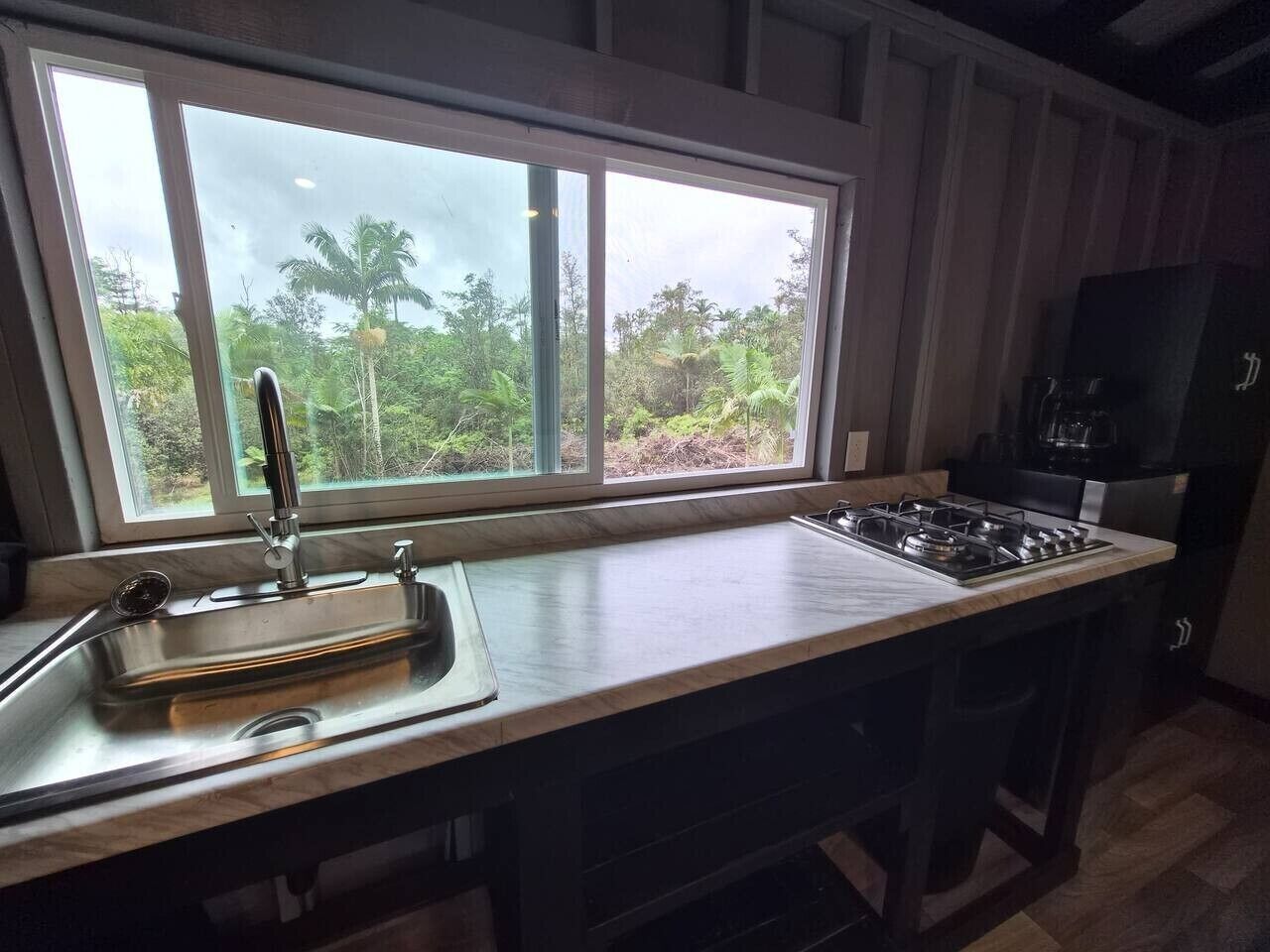 A kitchen with a large window, a stainless steel sink, and a gas stove.