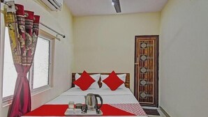 A hotel room with a bed, a window with curtains, a door with a decorative panel, and a ceiling fan. - sapphire guest house (Kolkata)