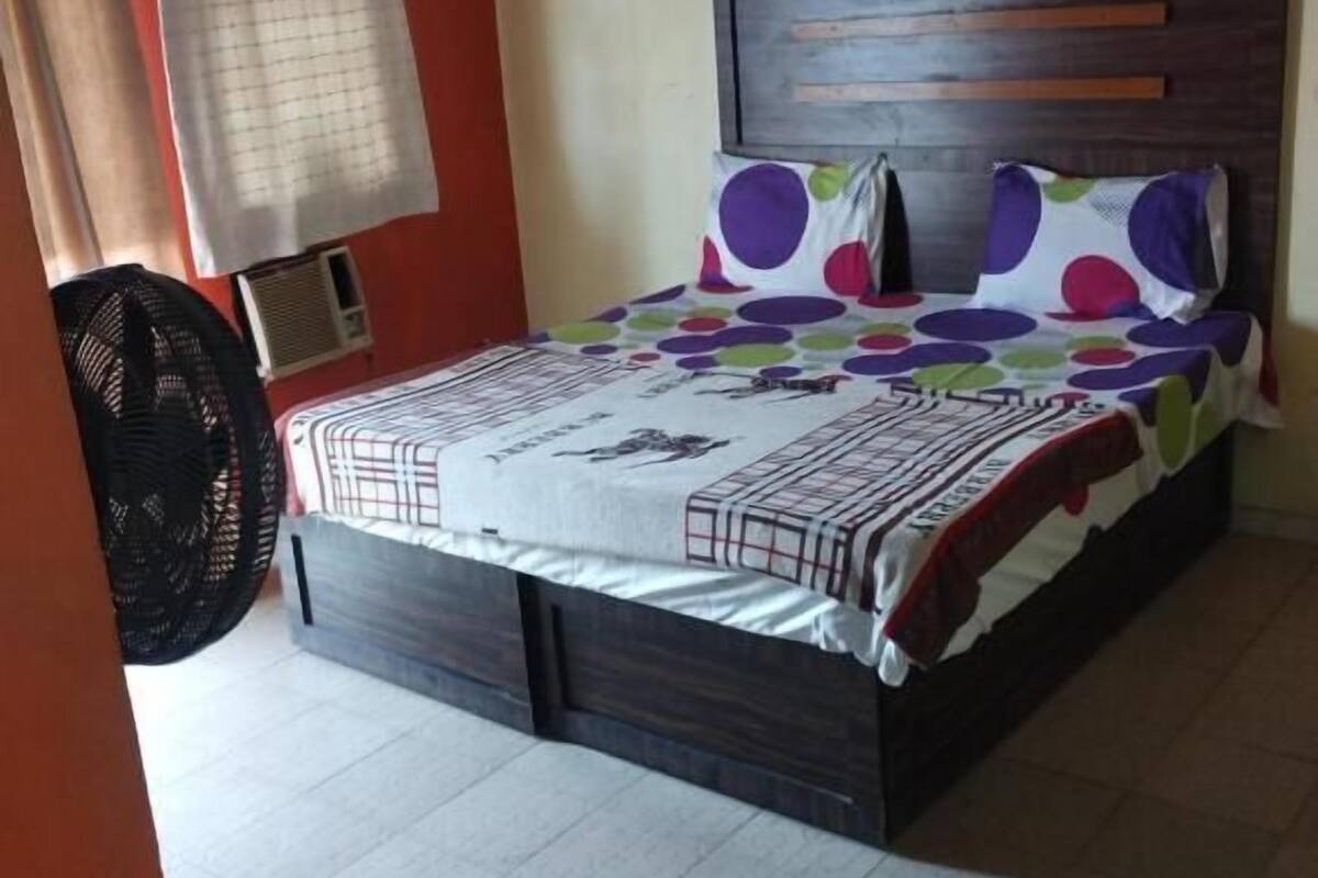 A bedroom with a bed, a headboard, a window with curtains, and a fan.