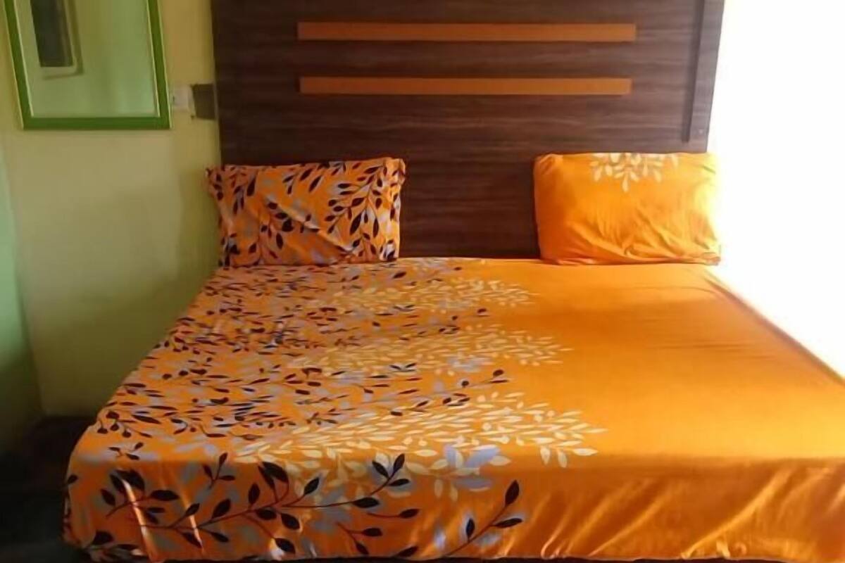 A bed with a patterned bedspread and two pillows, a wooden headboard, and a tiled floor with a geometric pattern.