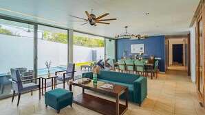 Ein geräumiger Wohnbereich mit Sofa, Couchtisch und Sesseln, ein Essbereich mit Tisch und Stühlen sowie ein großes Fenster mit Blick auf einen Pool.