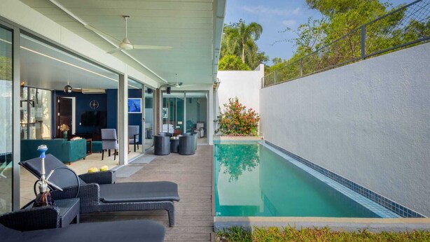 Ein Pool im Freien mit Liegestühlen, einem Fernseher und einem modernen Hausdesign.