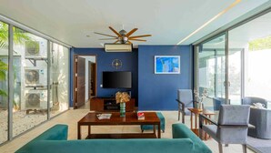 Ein modernes Wohnzimmer mit Deckenventilator, Flachbildfernseher, Couchtisch und blaugrünen Sofas.