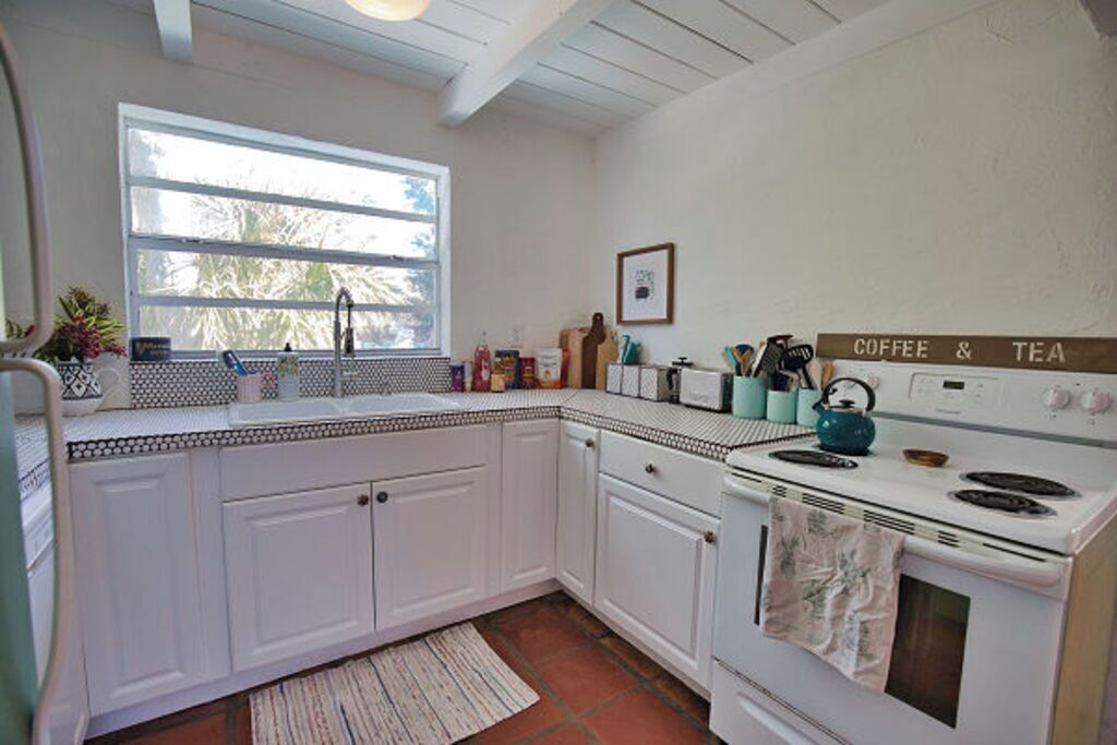 A kitchen with white cabinets, a stove, a sink, and a window.