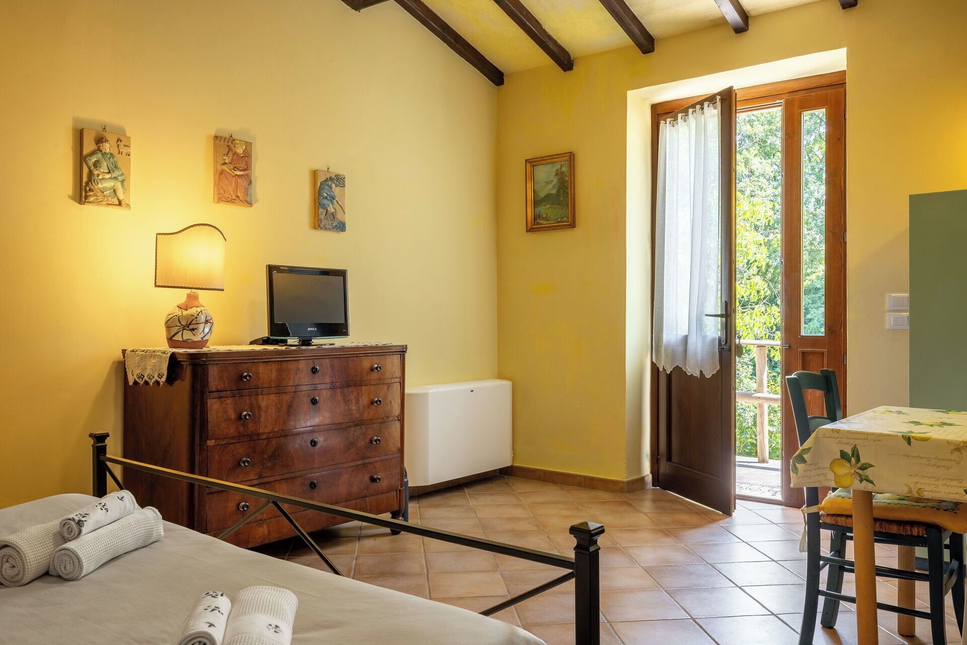 Een kamer met een bed, een houten dressoir, een televisie en een deur naar een buitenruimte.
