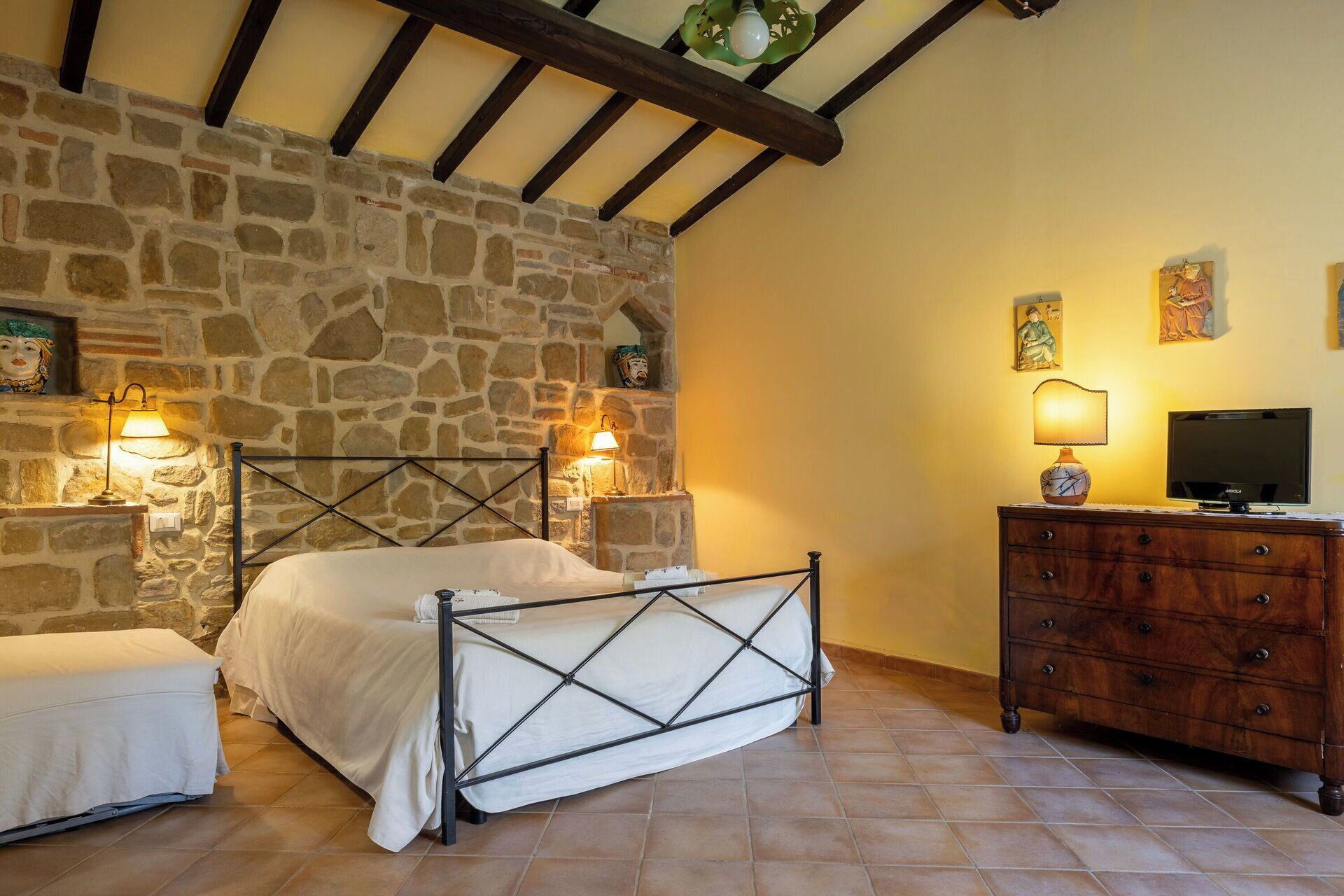 Un dormitorio con pared de piedra, una cama con estructura metálica, un aparador de madera y un televisor.
