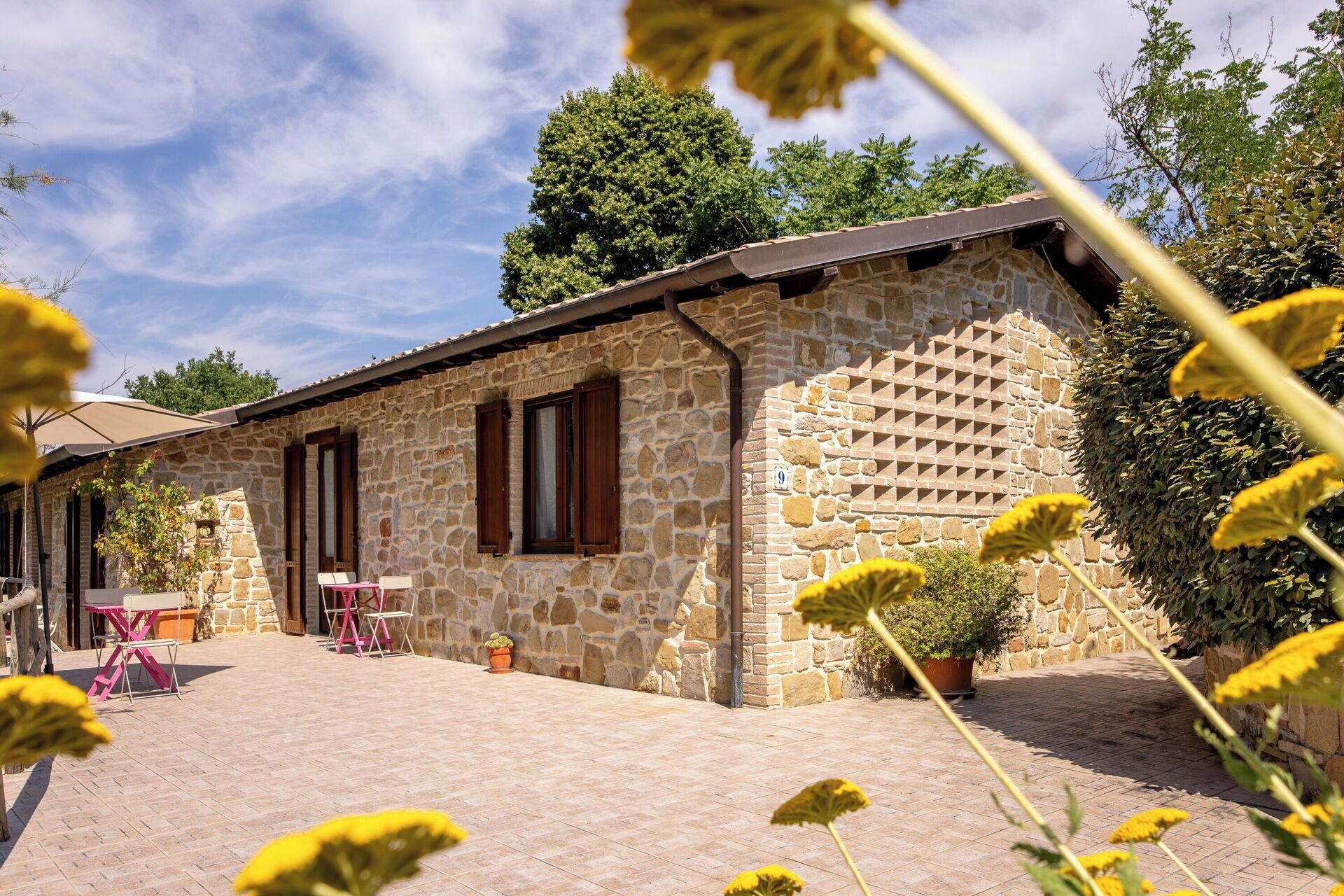 A stone building with a tiled patio, wooden shutters, and outdoor seating.