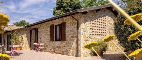 A stone building with a tiled patio, wooden shutters, and outdoor seating.