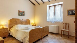 Ein Schlafzimmer mit einem hölzernen Bett, Nachttischlampen, einer Heizung, einem Fenster mit Vorhängen und einem Sessel.
