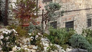 Un edificio de piedra con varias ventanas, techo de metal y un jardín con diversas plantas.