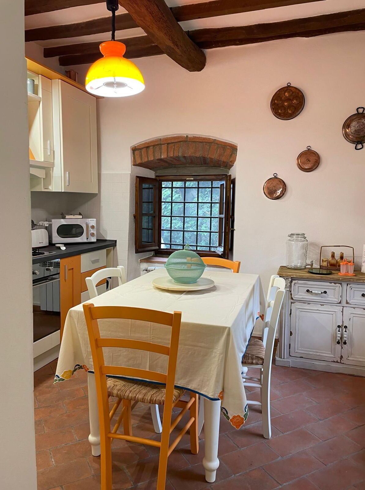 A dining area with a table set for four, a window with a view, and a kitchen with white cabinets and a microwave.