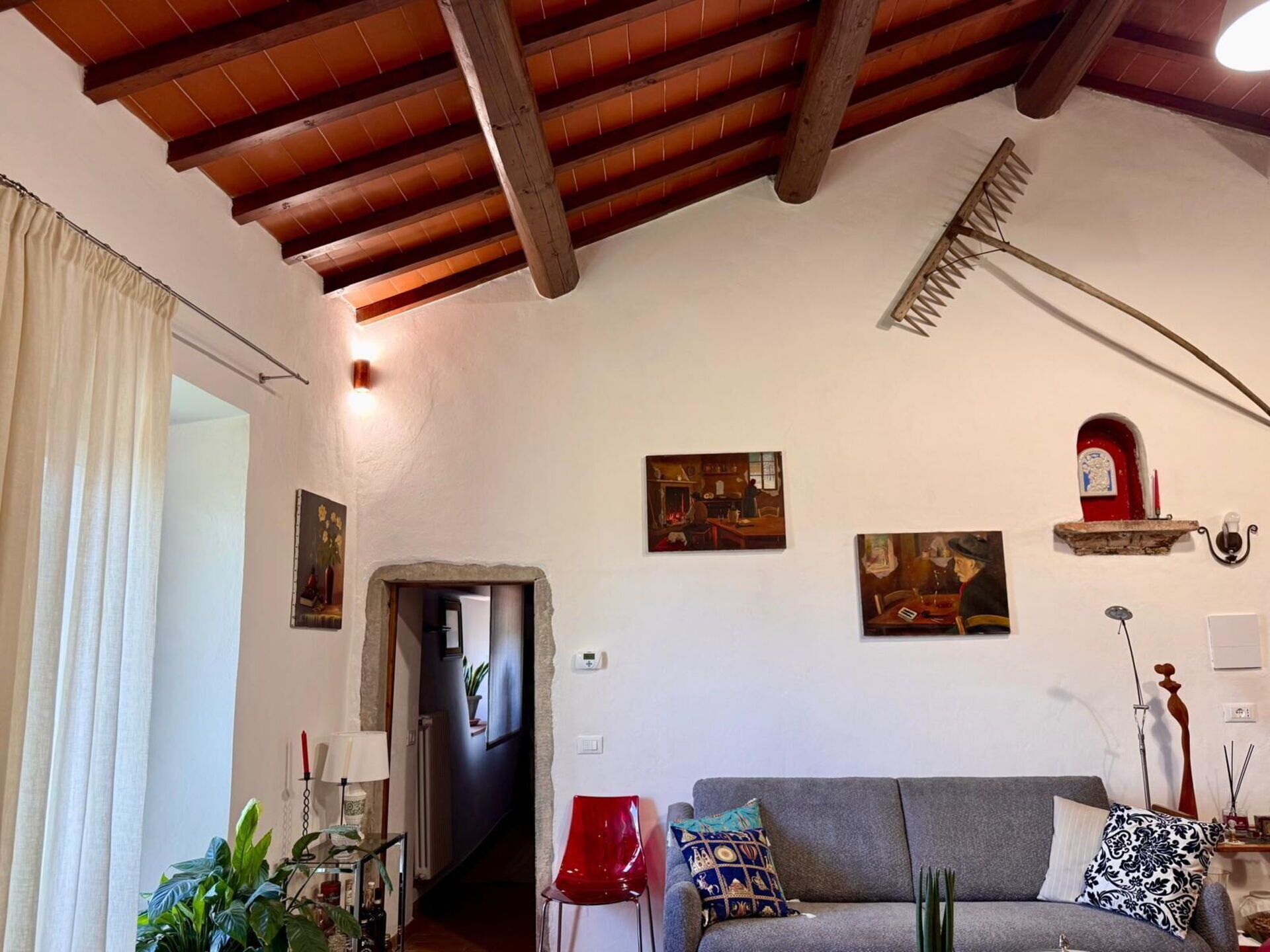 A living room with a wooden ceiling, a grey sofa, a red chair, and a staircase leading to another room.