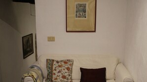 A room with a white sofa, a framed picture on the wall, and a wooden table in the center. - House pe'L Ghetto (Pitigliano)