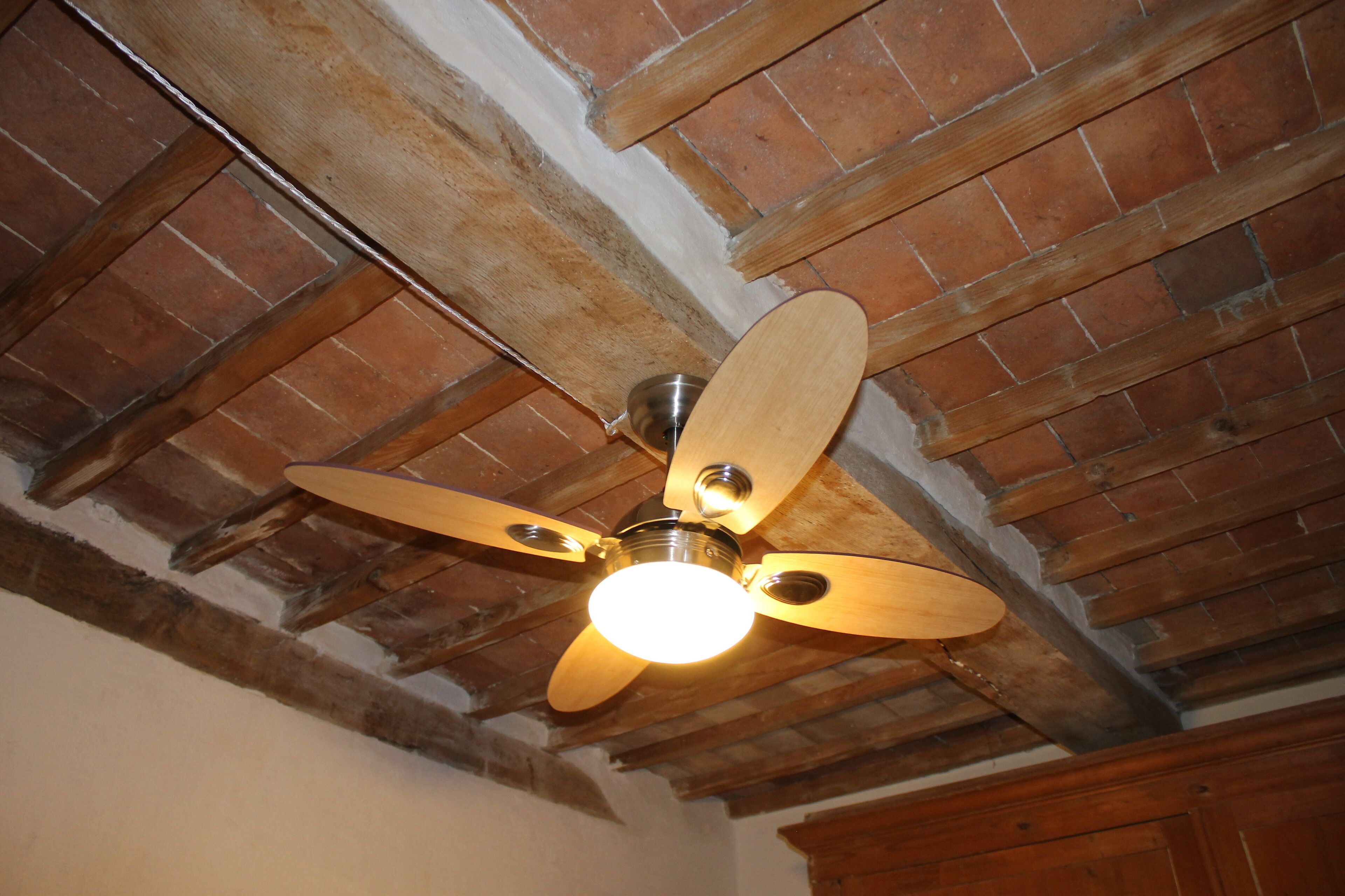 Ein Deckenventilator mit vier Flügeln, eine Leuchte und freiliegende Holzbalken.