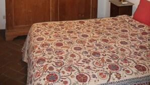 A bedroom with a wooden wardrobe, a bed with a patterned bedspread, a ceiling fan, and a small bedside table with a lamp. - House pe'L Ghetto (Pitigliano)
