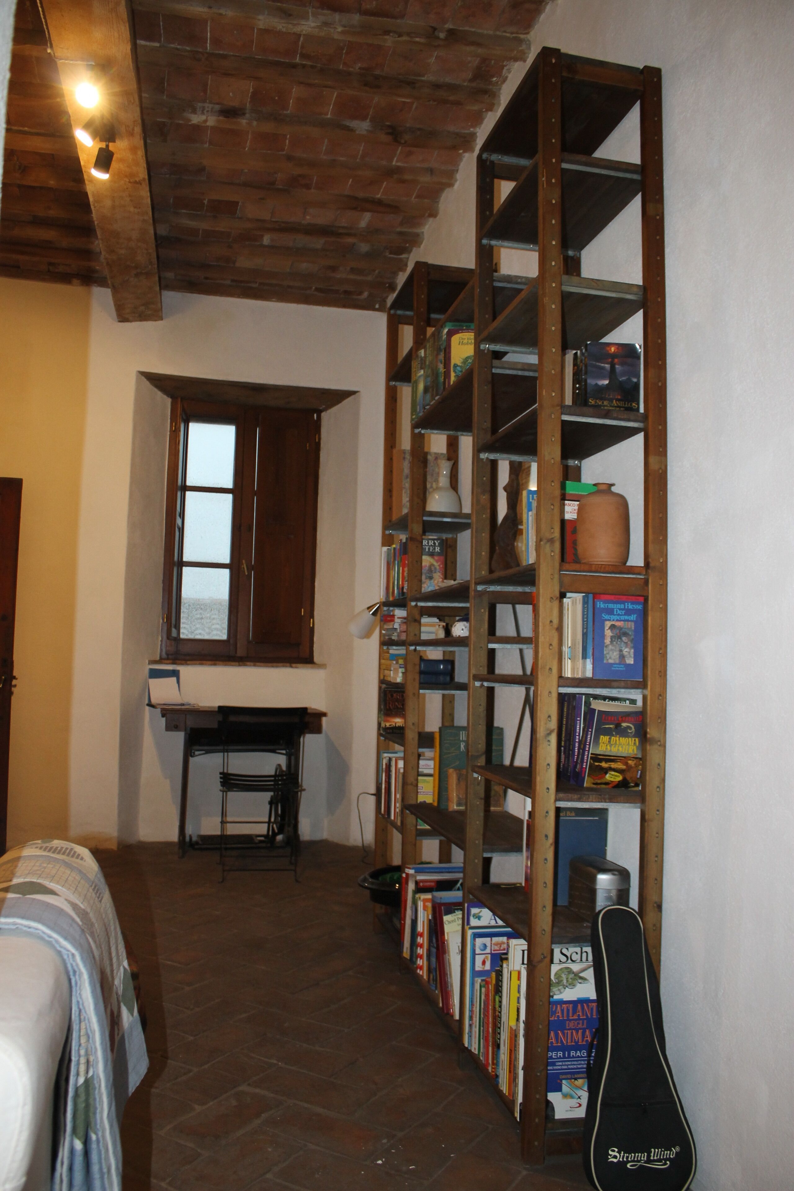 Una habitación estrecha con techo de ladrillo, una estantería de madera, una ventana y una guitarra.