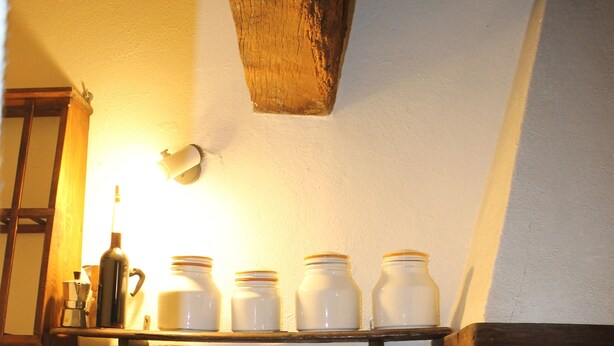 A kitchen with a shelf holding jars, a hanging light, and a tiled backsplash. - House pe'L Ghetto (Pitigliano)