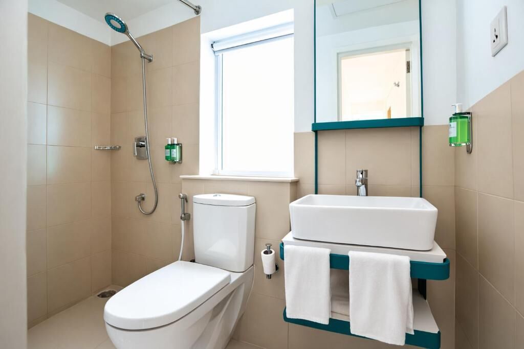 A bathroom with a toilet, shower, sink, and a window.
