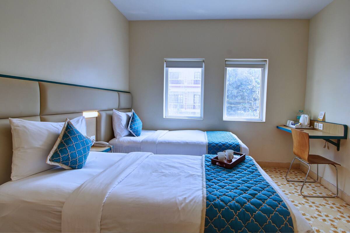Ein Hotelzimmer mit zwei Betten, einem Schreibtisch und zwei Fenstern.