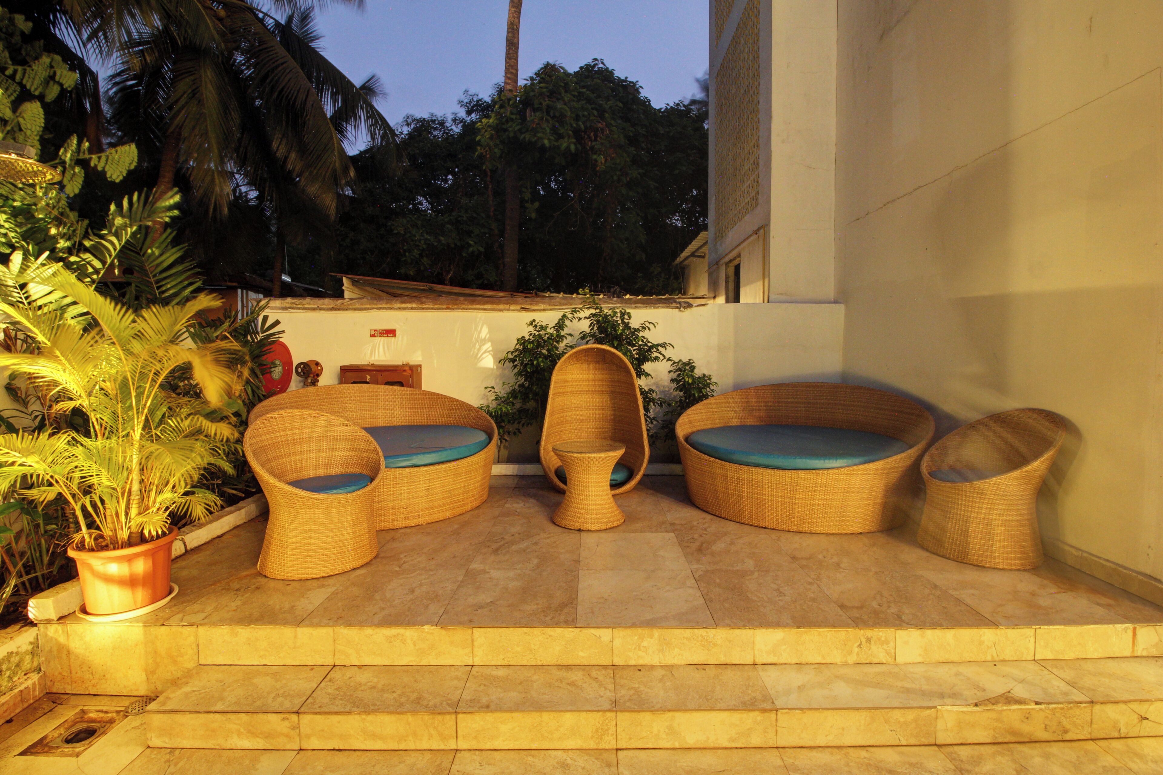 A patio with wicker furniture, a potted plant, and a building in the background.