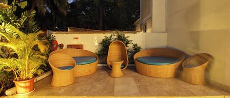 A patio with wicker furniture, a potted plant, and a building in the background.