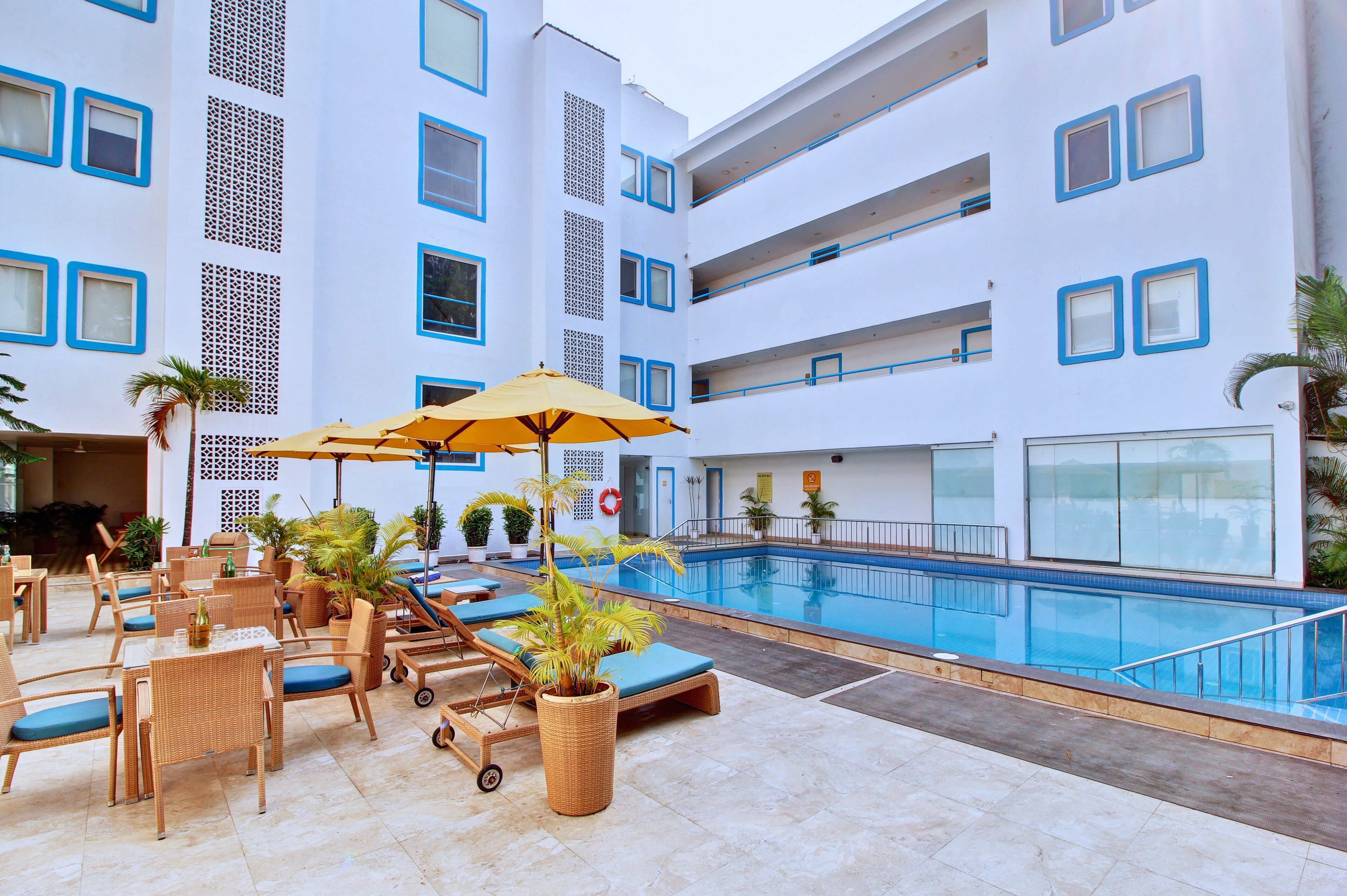 Un hotel con piscina, mobiliario exterior con sombrillas y plantas en macetas.
