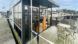 Un bateau moderne doté d’un habitacle entièrement vitré, d’un pont avec une table et des chaises, et offrant une vue sur les autres bateaux en arrière-plan.