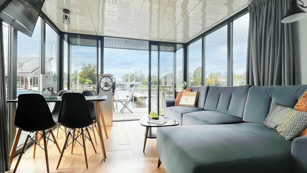 Un salon moderne doté d’un grand canapé, d’une table à manger avec des chaises et de grandes fenêtres offrant une vue sur l’extérieur.