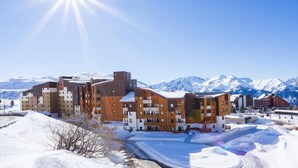 A multi-story building with a modern architectural design, featuring balconies and a snow-covered landscape with mountains in the background.