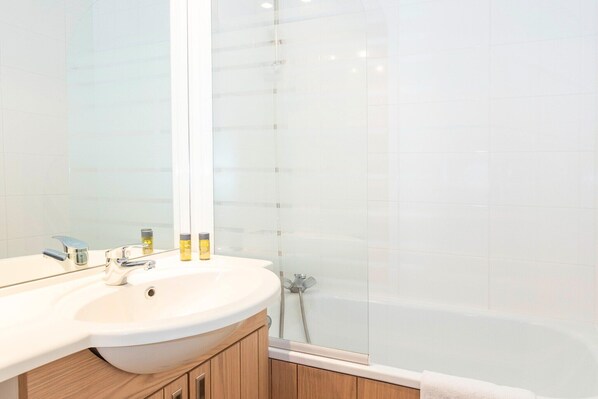 Un baño moderno con un espejo grande, un lavamanos blanco y una ducha con mampara de vidrio.
