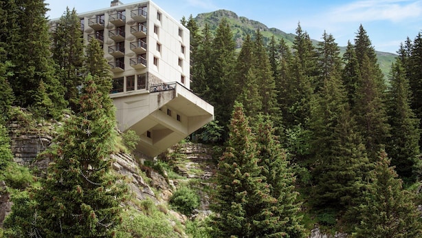 Ein modernes Gebäude mit Balkonen, umgeben von dichtem Wald und Bergen.