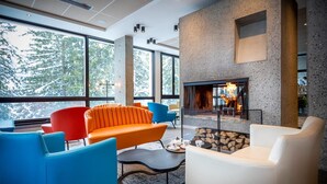 Ein moderner Loungebereich mit Kamin, großen Fenstern und farbenfroher Sitzmöbel.